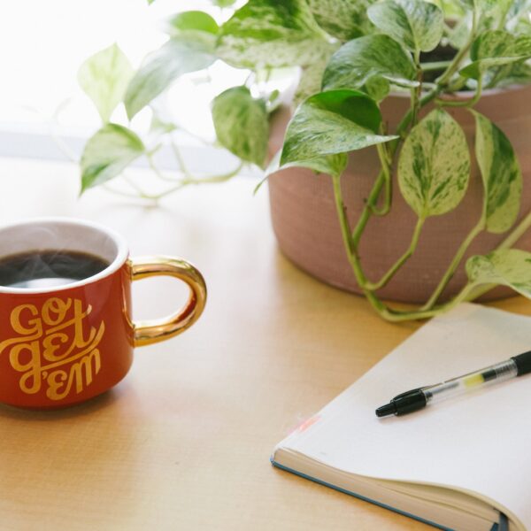 black retractable pen on opened book beside red and white go get'em-printed coffee cup