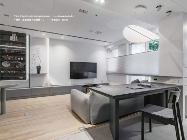 Contemporary living room with wall-mounted TV, glass display cabinet, and gray sectional sofa on light wood floors; dining table in foreground.