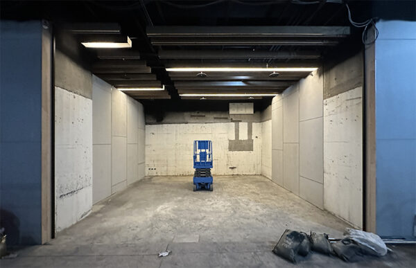 Blue scissor lift centered in a large empty industrial bay with concrete walls and overhead lighting.