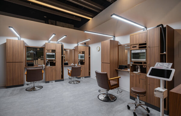 Modern hair salon interior with several wood-paneled styling stations, brown chairs, mirrors, and bright linear lighting.