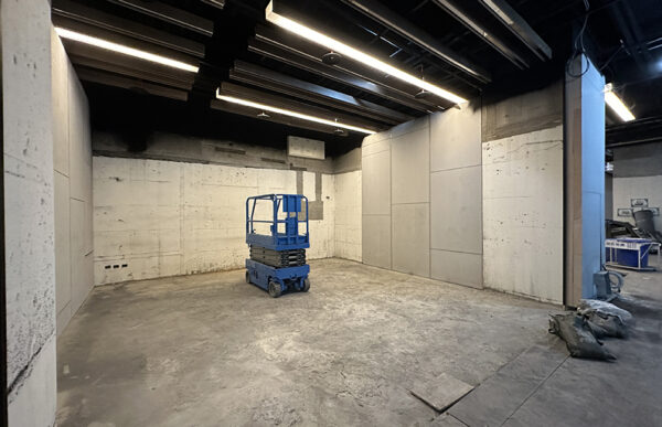 Blue scissor lift parked in an empty concrete construction room with overhead lights in use by the site? (informational)